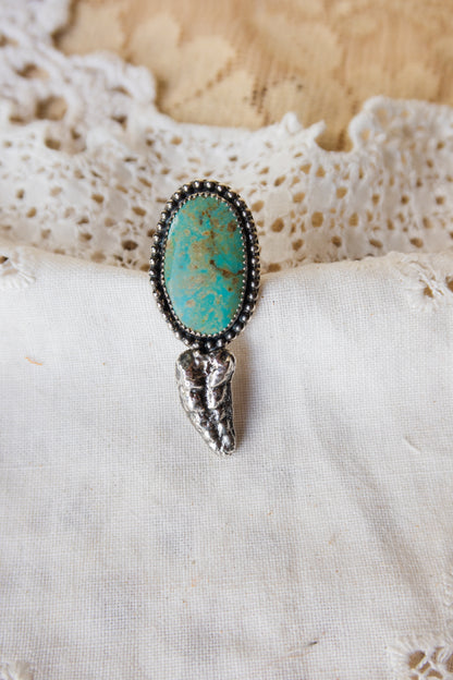 This one-of-a-kind Sterling Silver Turquoise Rattler Ring is handcrafted in the heart of South Texas. This whimsical beauty features a striking double ring shank design that wraps around your finger like a coiled serpent, crowned with genuine Kingman turquoise that captures the wild spirit of the south Texas Terrain. Each piece is uniquely crafted, making it a treasure that's as individual as you are.&nbsp;