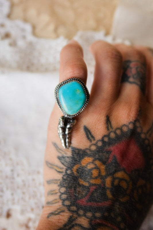This one-of-a-kind Sterling Silver Turquoise Rattler Ring is handcrafted in the heart of South Texas. This whimsical beauty features a striking double ring shank design that wraps around your finger like a coiled serpent, crowned with genuine Kingman turquoise that captures the wild spirit of the south Texas Terrain. Each piece is uniquely crafted, making it a treasure that's as individual as you are.&nbsp;