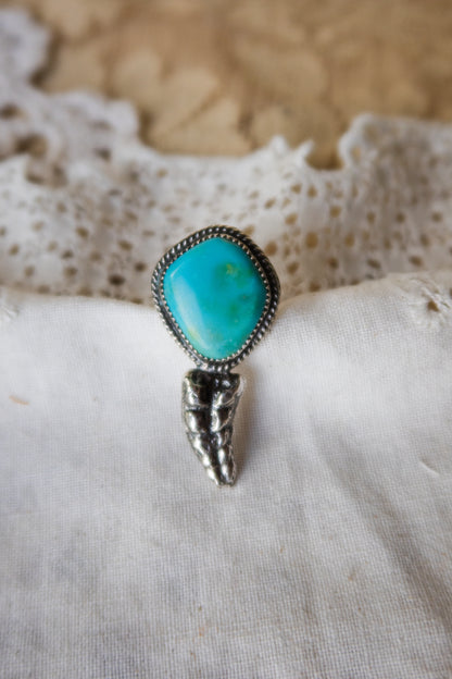This one-of-a-kind Sterling Silver Turquoise Rattler Ring is handcrafted in the heart of South Texas. This whimsical beauty features a striking double ring shank design that wraps around your finger like a coiled serpent, crowned with genuine Kingman turquoise that captures the wild spirit of the south Texas Terrain. Each piece is uniquely crafted, making it a treasure that's as individual as you are.&nbsp;