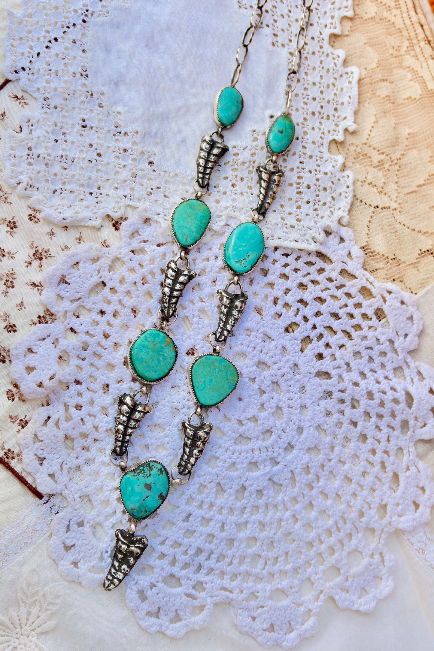 This striking pendant features seven vibrant Sonoran turquoise stones paired with seven solid sterling silver sand cast rattlers, each cast from an authentic rattlesnake sourced in south Texas. The turquoise stones are complemented by a handmade sterling silver chain, creating a one-of-a-kind piece that celebrates the raw beauty of South Texas. Each rattler is individually cast, ensuring no two necklaces are identical. The combination of natural turquoise and sculptural silver elements makes this pendant a 