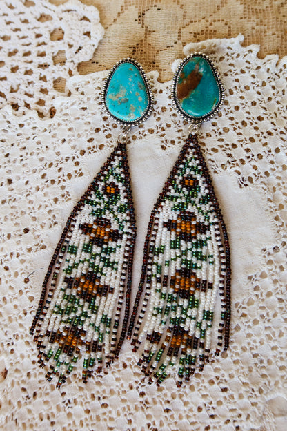 Bloom where you're beaded! These whimsical Sterling Silver and Turquoise Beaded Floral Earrings bring a touch of Southwestern charm to your everyday style. Each pair is meticulously hand-beaded with vibrant turquoise stones, creating delicate floral designs that dance with every movement. Handcrafted with love in South Texas, these earrings are a celebration of uniqueness and eccentric style. Perfect for adding a pop of color and personality to any outfit.