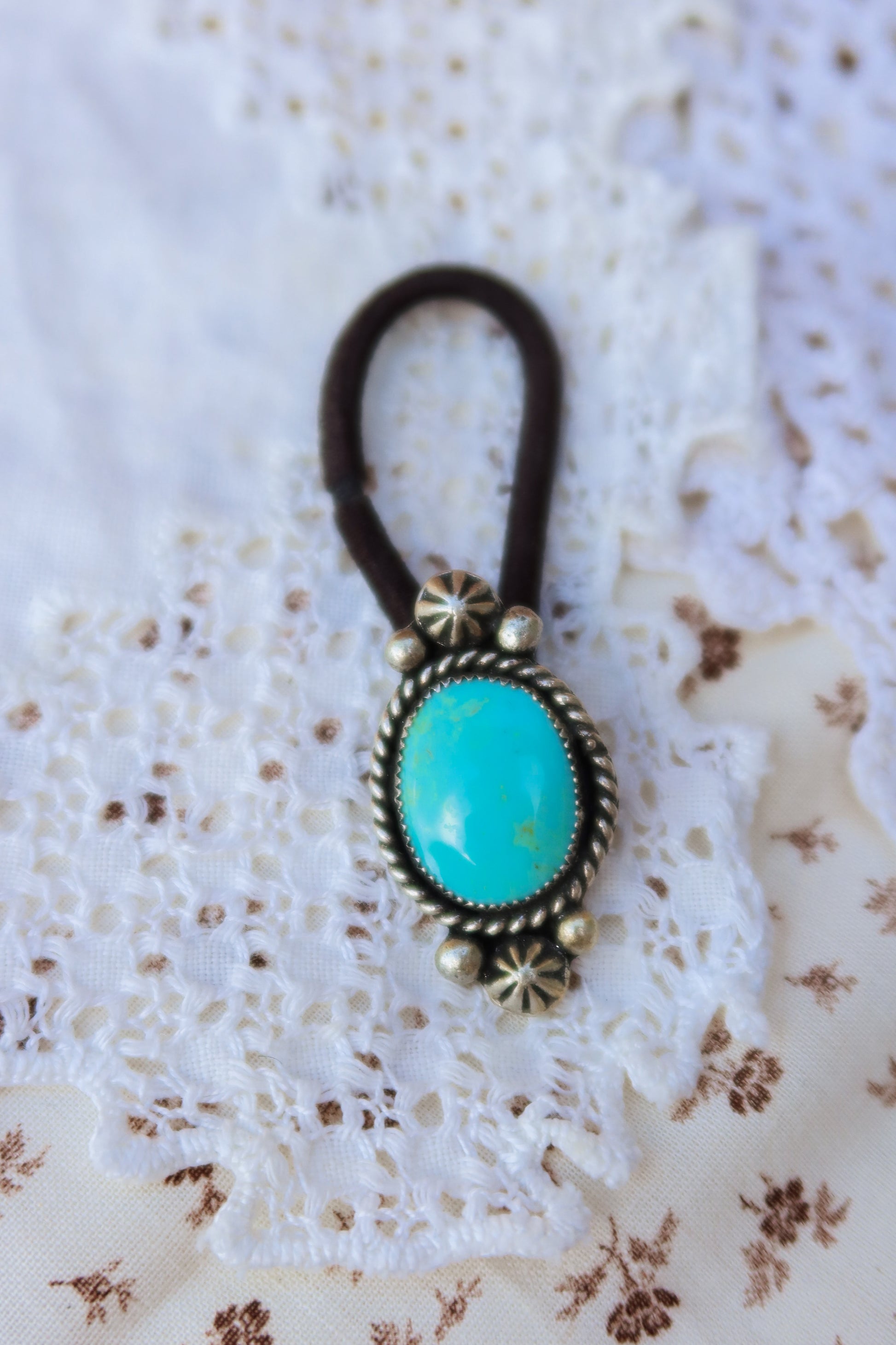 Elevate your everyday style with this stunning hair tie featuring genuine Sonoran turquoise with sterling silver ornaments. Available in three versatile options to match your look: Black, Brown, or blonde. Perfect for securing your hair while making a statement.&nbsp;