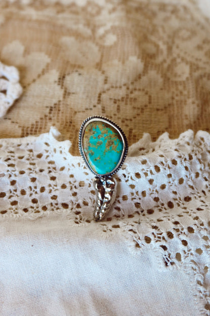 This one-of-a-kind Sterling Silver Kingman Turquoise Rattler Ring is handcrafted in the heart of South Texas. This whimsical beauty features a striking double ring shank design that wraps around your finger like a coiled serpent, crowned with genuine Kingman turquoise that captures the wild spirit of the south Texas Terrain. Each piece is uniquely crafted, making it a treasure that's as individual as you are.