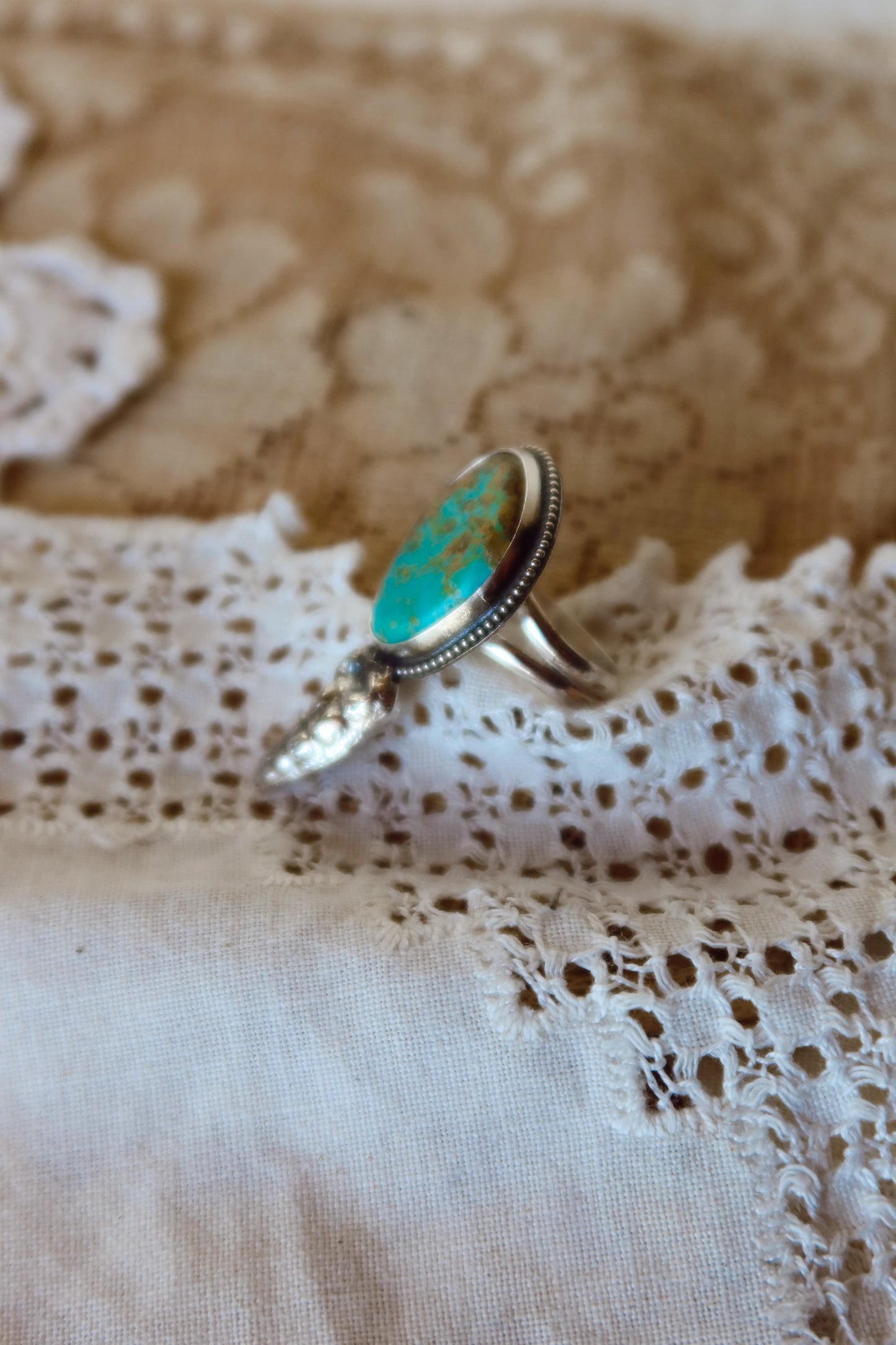 This one-of-a-kind Sterling Silver Kingman Turquoise Rattler Ring is handcrafted in the heart of South Texas. This whimsical beauty features a striking double ring shank design that wraps around your finger like a coiled serpent, crowned with genuine Kingman turquoise that captures the wild spirit of the south Texas Terrain. Each piece is uniquely crafted, making it a treasure that's as individual as you are.