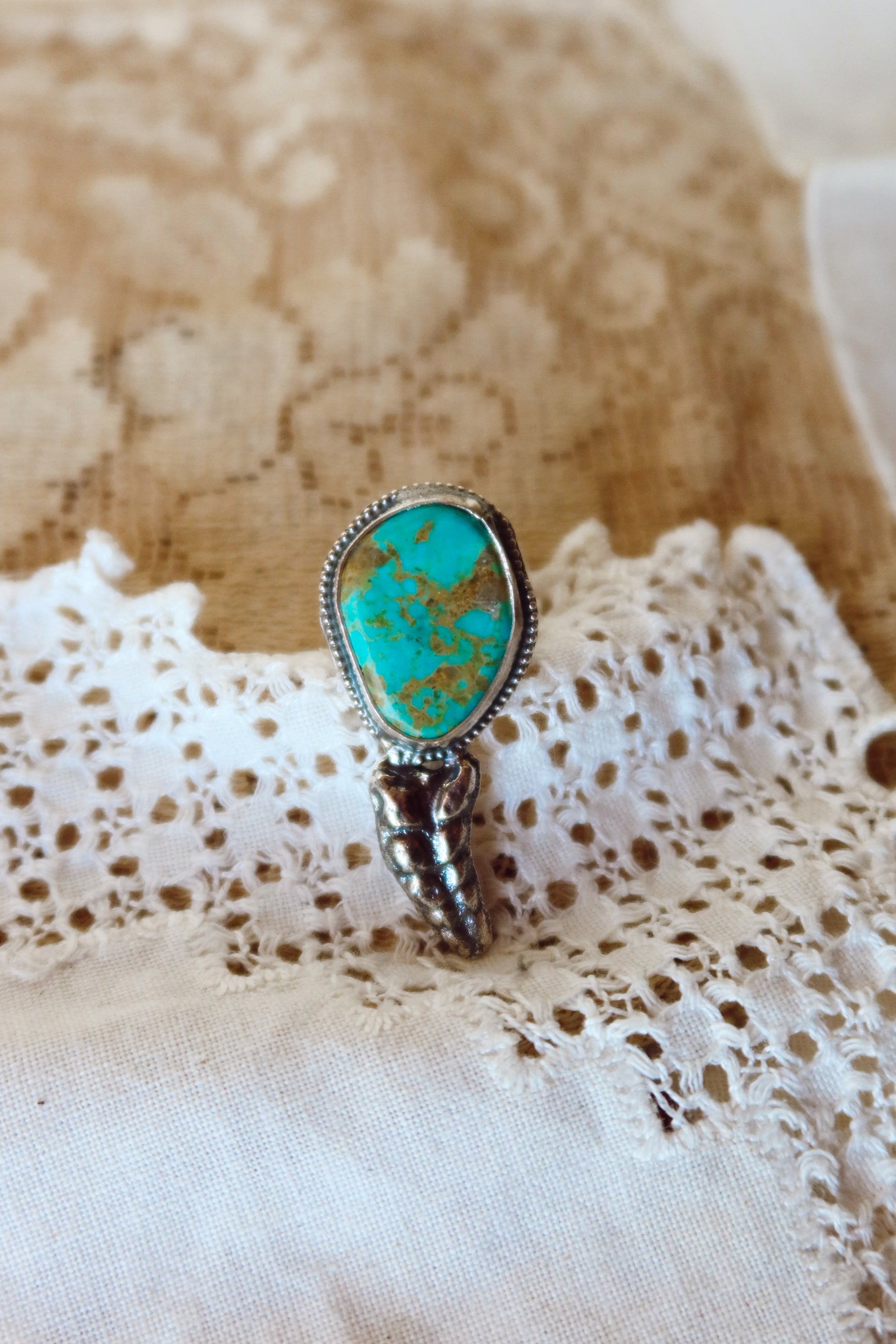  This one-of-a-kind Sterling Silver Kingman Turquoise Rattler Ring is handcrafted in the heart of South Texas. This whimsical beauty features a striking double ring shank design that wraps around your finger like a coiled serpent, crowned with genuine Kingman turquoise that captures the wild spirit of the south Texas Terrain. Each piece is uniquely crafted, making it a treasure that's as individual as you are.