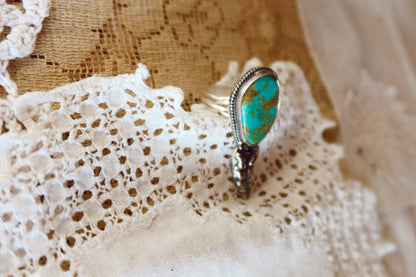 This one-of-a-kind Sterling Silver Kingman Turquoise Rattler Ring is handcrafted in the heart of South Texas. This whimsical beauty features a striking double ring shank design that wraps around your finger like a coiled serpent, crowned with genuine Kingman turquoise that captures the wild spirit of the south Texas Terrain. Each piece is uniquely crafted, making it a treasure that's as individual as you are.